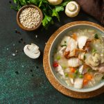 Healthy eating. Homemade hearty soup with cereals, bacon and mushrooms on a dark stone background.