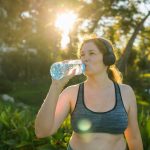 Overweight woman drinking water after jogging in the park. Portrait of young plus-size thirsty woman