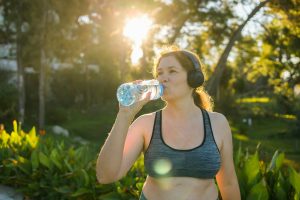 Overweight woman drinking water after jogging in the park. Portrait of young plus-size thirsty woman